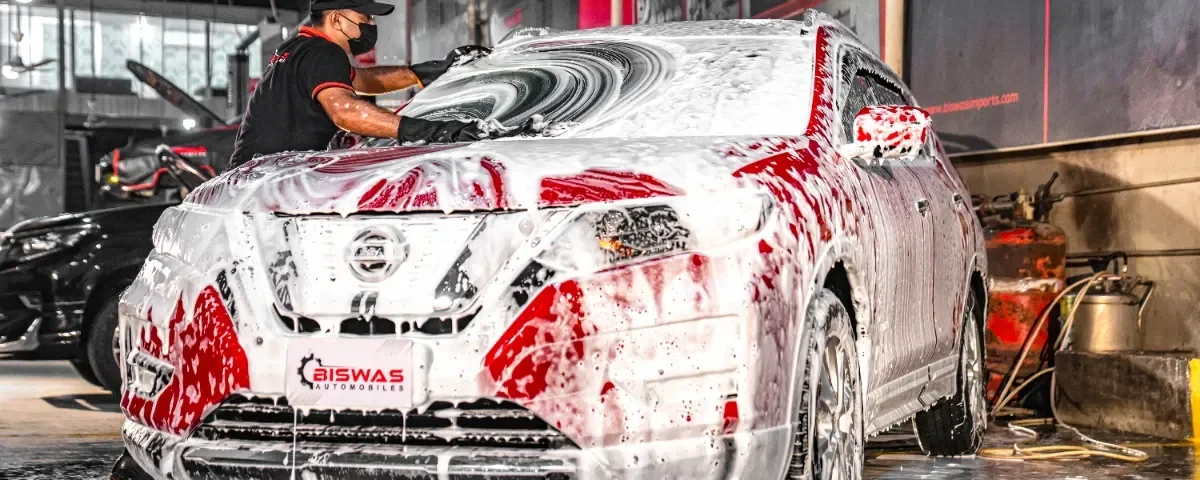 A technician cleaning a car with foam at Biswas Automobiles, showcasing high-quality car wash services in Dhaka.